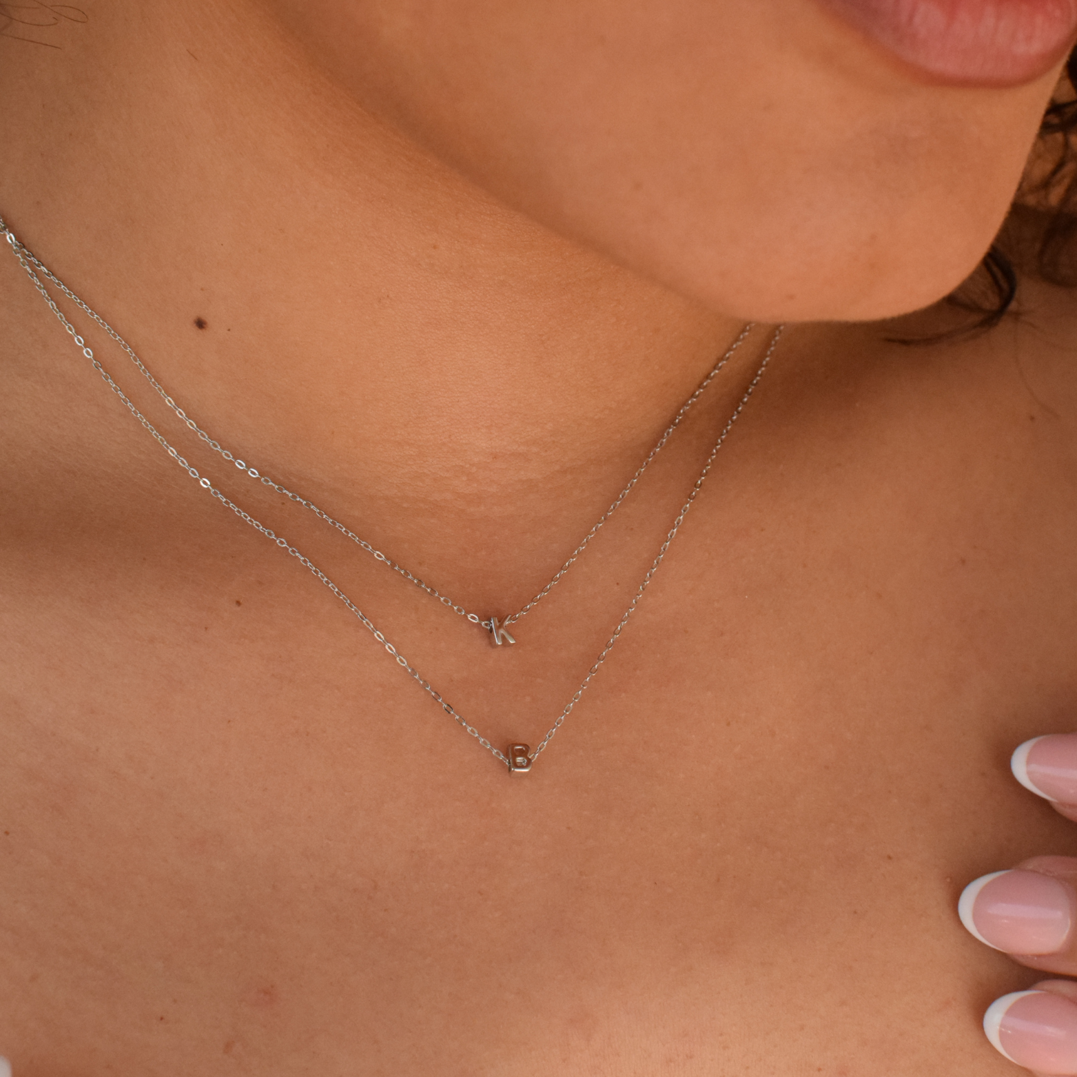 Close-up of a woman wearing two initial necklaces made of sterling silver necklace 
