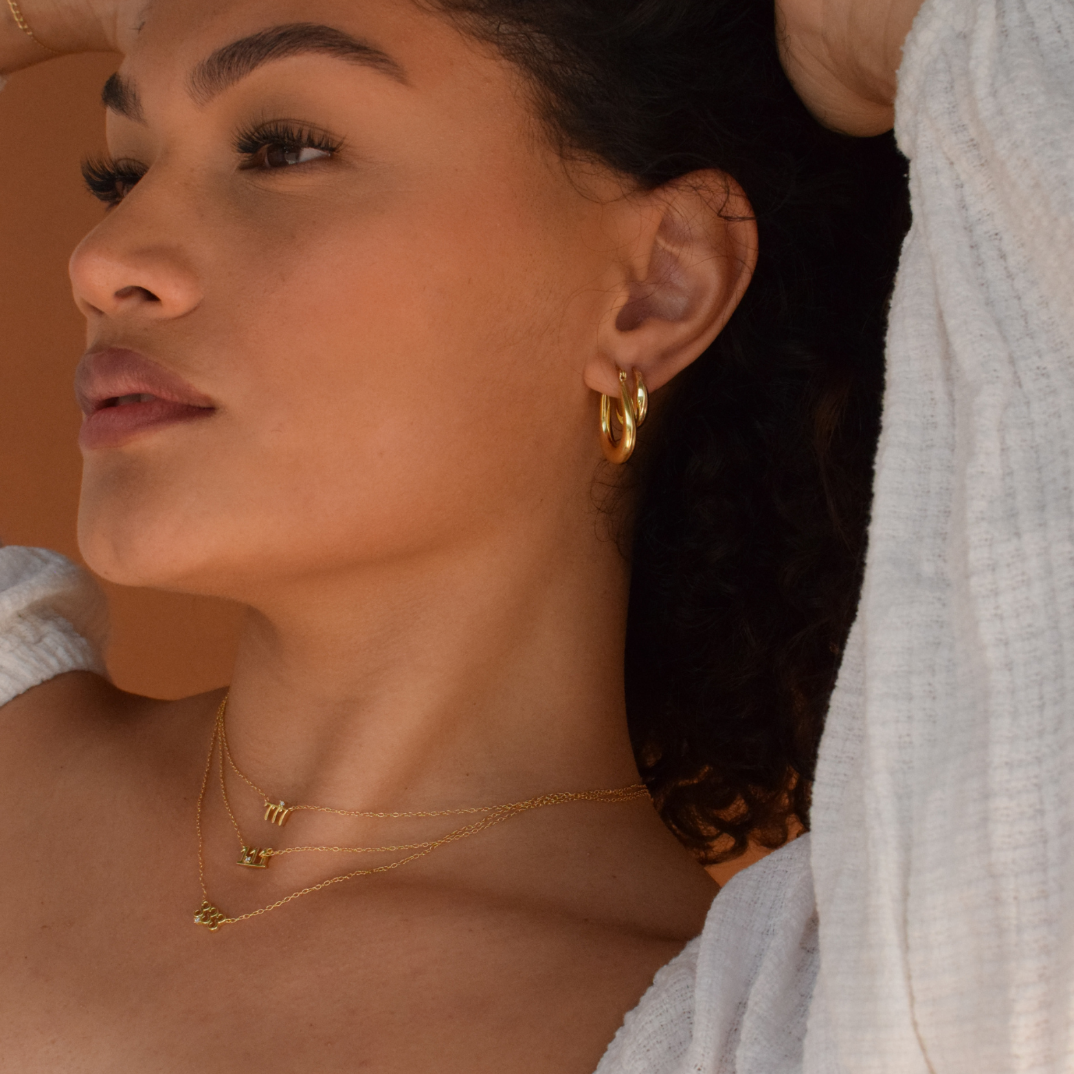 Close-up of a woman wearing 'Isla Hoops' 14K Gold Plated earrings with her curly hair