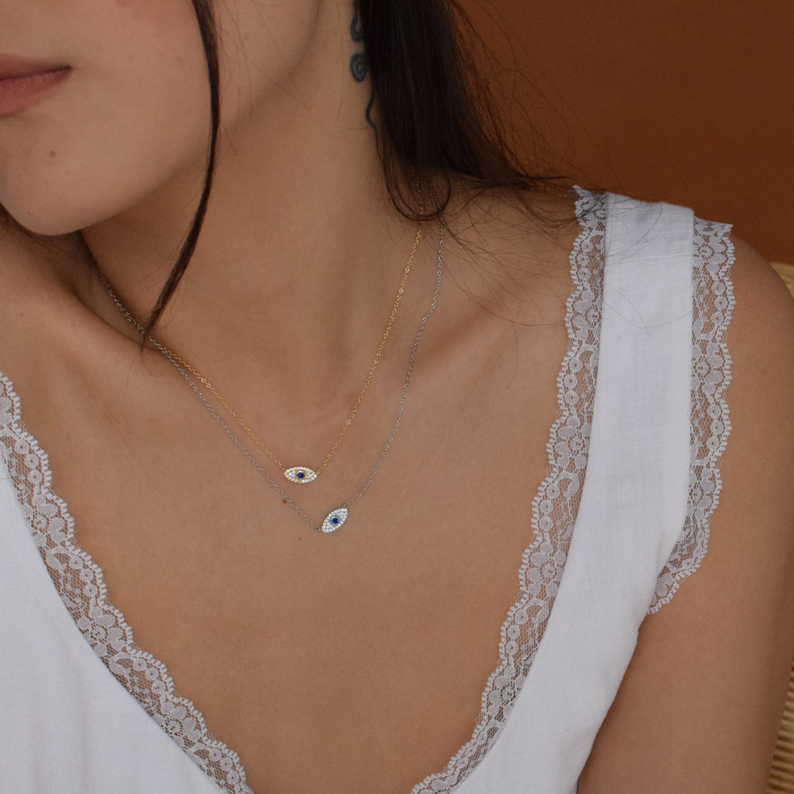 Woman in a white top showcasing the Iris Necklace with a blue evil eye charm