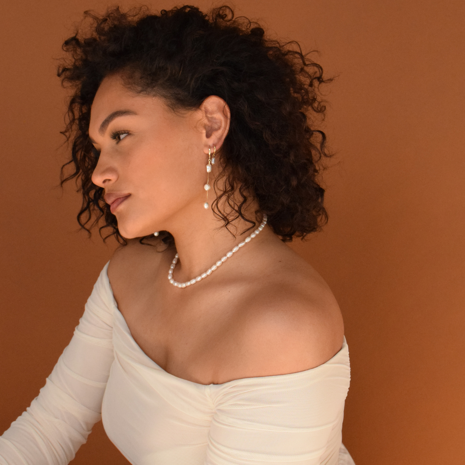 Woman with curly hair showcasing the Baroque Hoops - 14K Gold Plated with a coordinating white outfit