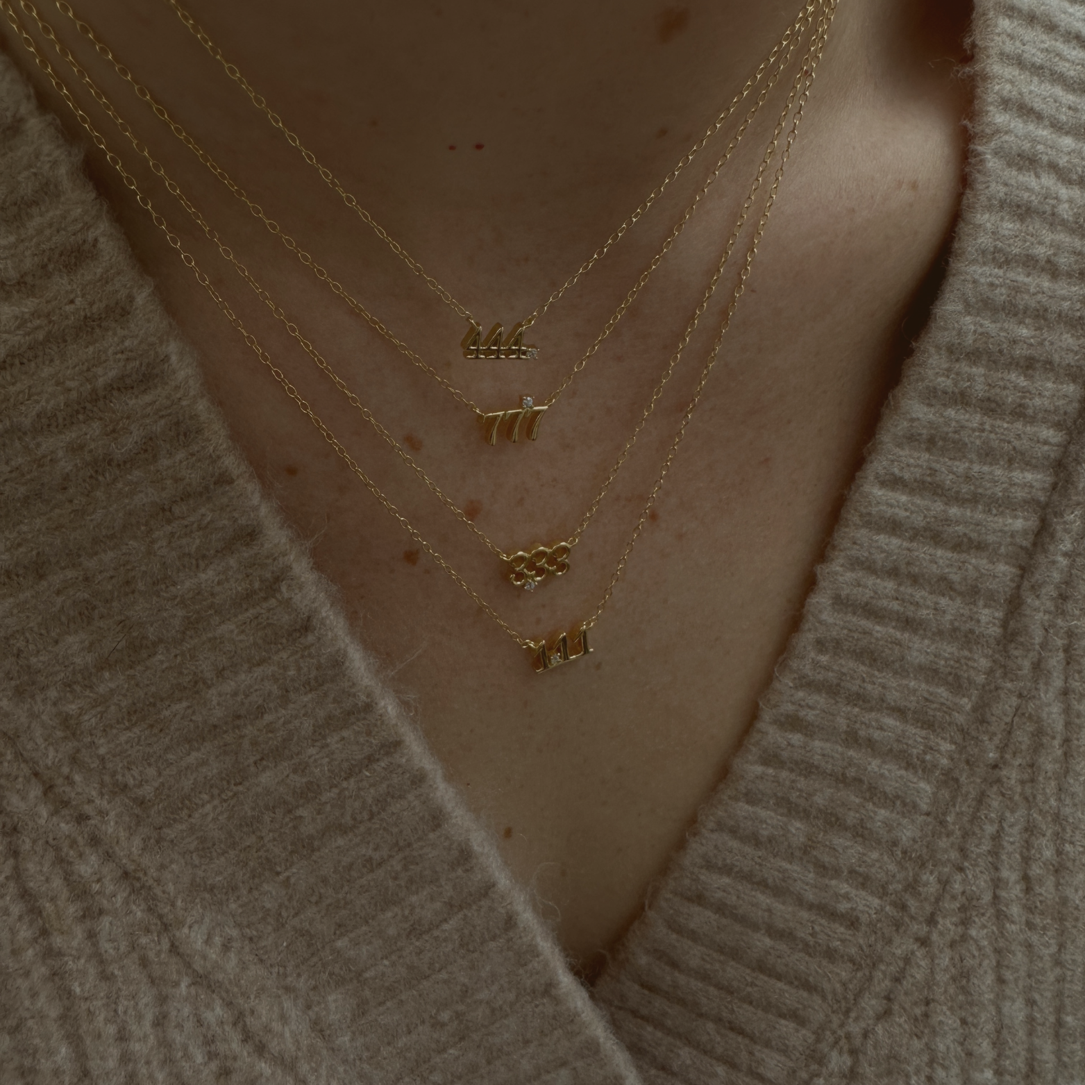 Close-up of a 14K gold-plated angel number 444 necklace with the rest of the collection