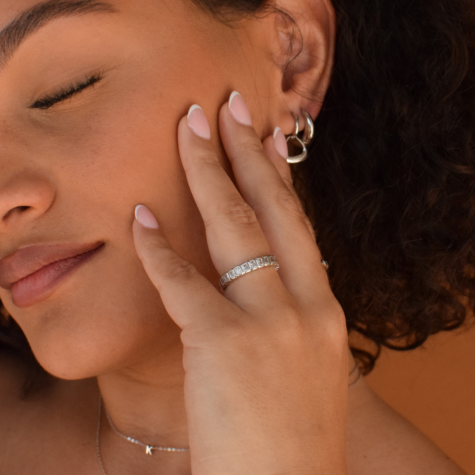 Athena Hoops sterling silver earrings on a woman's ear with additional jewelry on her hand
